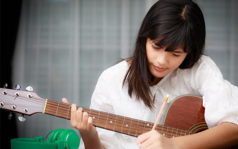 woman practicing on guitar writes down notes